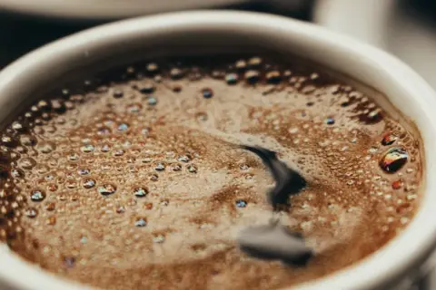 En vit kopp med bubbligt java kaffe. Skummet har regnbågsskimrande bubblor och en mörk virvel i mitten.