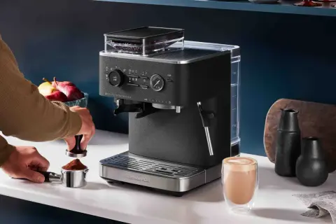 En person förbereder espresso i en kaffebryggare. En färdigbryggd latte står bredvid.