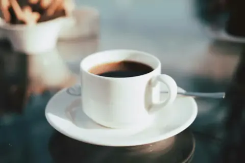 En kopp med **temp rostas** kaffe står på ett fat. I bakgrunden syns en skål med kex.