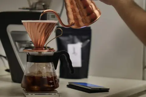 En person häller varmt vatten över kaffepulver i en kopparfilterhållare för att brygga kaffe manuellt.