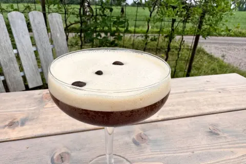 En härlig espresso martini med krämigt skum och tre kaffebönor, perfekt för en stunds avkoppling utomhus.