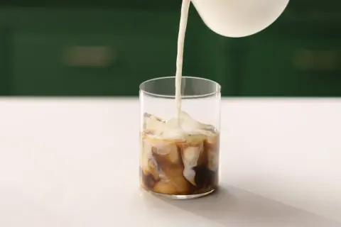 Mjölk hälls i ett glas med is och kaffe. Ett perfekt iskaffe recept för en varm dag.