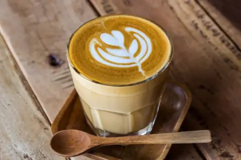 En vacker latte med mjölkskum som bildar ett mönster, serverad med en träsked. Perfekt kaffe för en mysig stund.