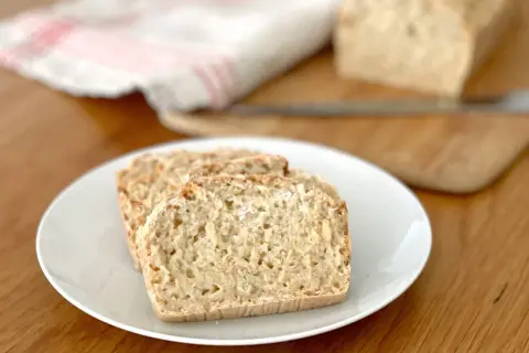 Tre skivor glutenfri limpa på en vit tallrik. En hel limpa syns i bakgrunden.