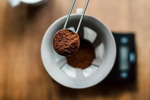 Malen kaffepulver hälls från en skopa ner i en filterhållare, redo för bryggning. Rätt kaffe temperatur är avgörande för smaken.