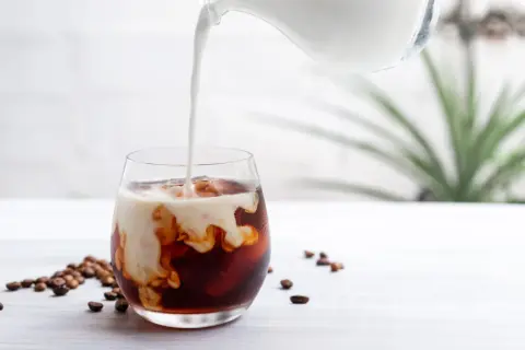 Mjölk hälls i ett glas med iskaffe och kaffebönor, en perfekt islatte.
