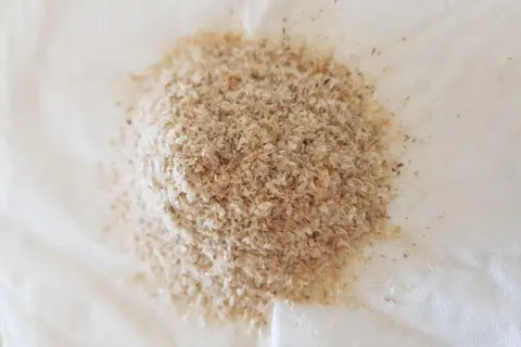 En hög med ljusbrunt fiberhusk, som ser ut som små, tunna flingor, ligger på en vit yta.