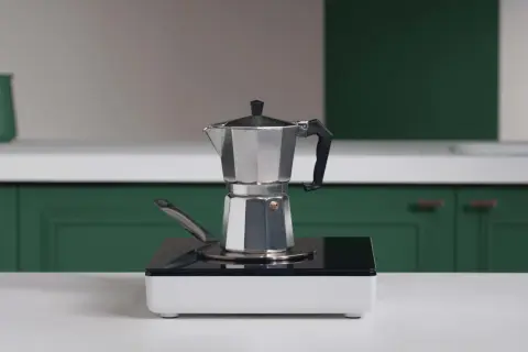 En mokkakanne står på en induktionshäll, redo att koka kaffe på spis.