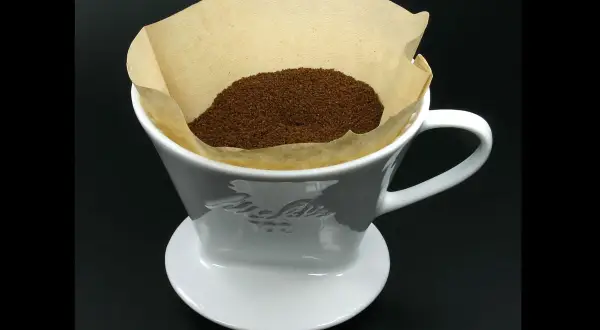 En vit kaffefilterhållare med kaffepulver i ett pappersfilter. Vem uppfann kaffefiltret? Melitta Bentz 1908.