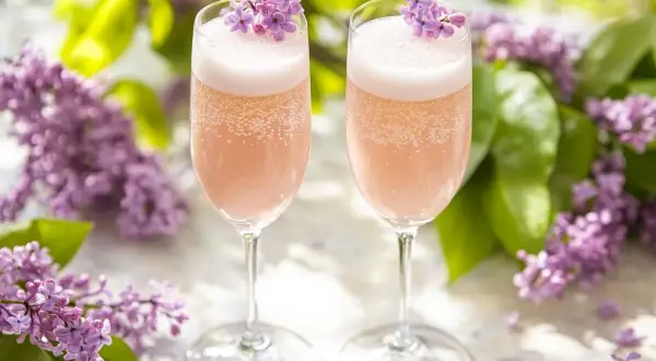 Två glas med rosa bubbel, dekorerade med syrenblommor. Perfekt för ett syrensirap recept en solig dag.