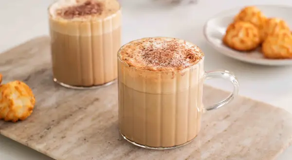 Två glas med krämiga kaffedrinkar, toppade med kanel och en liten tallrik med makroner. Perfekt för inspiration till egna kaffedrinkar recept.