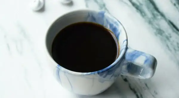En kopp kaffe, perfekt för att njuta av ditt americano recept. Vita hörlurar ligger bredvid.