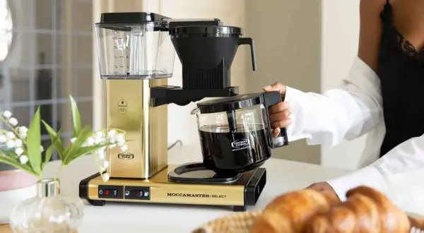 En guldfärgad Moccamaster kaffebryggare med en glaskanna fylld med kaffe. Denna modell är känd för sin optimala bryggtemperatur.