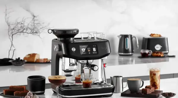 Svart espressomaskin med kaffekoppar, chokladbitar och en glasburk med iskaffe. Perfekt för att brygga gott kaffe oavsett om du har hårt eller mjukt vatten.