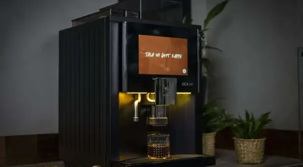 Svart kaffemaskin brygger en kopp kaffe, med texten "Tala om gott kaffe" på skärmen. Perfekt för dig som vill ha exakt rätt mängd gram kaffe per kopp.