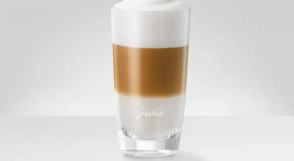 En perfekt lagerdelad latte macchiato i ett glas med Jura-logotyp.