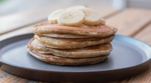 En hög med fluffiga bananpannkakor, toppad med bananskivor. Ett enkelt och gott bananpannkaka recept för frukost eller mellanmål.