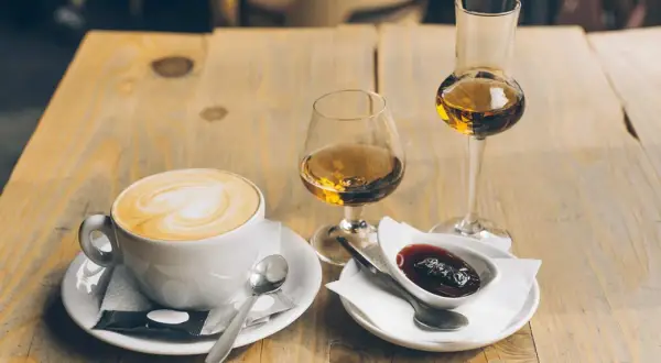 En kopp cappuccino med hjärtkonst, två glas avec och en skål med sylt. Perfekt avec till kaffet.