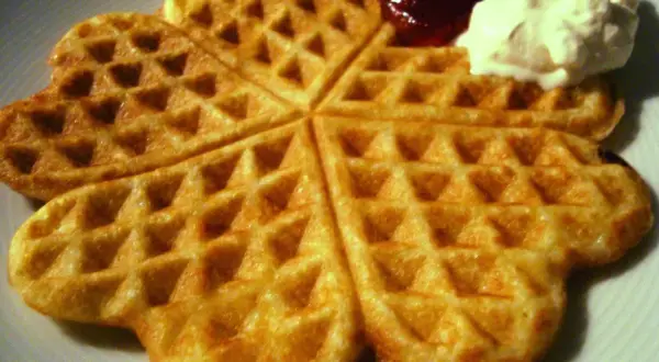 Golden-brown heart-shaped waffles with jam and whipped cream.