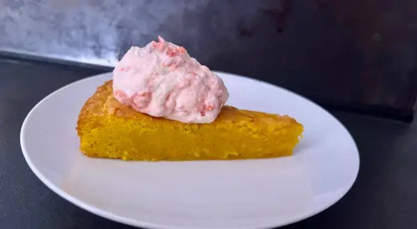En bit glutenfri saffranskladdkaka med vit choklad, toppad med rosa grädde.