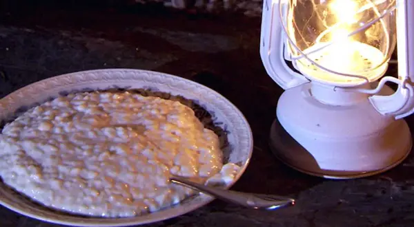 En skål med krämig risgrynspudding med bittermandel, belyst av en vit oljelampa.