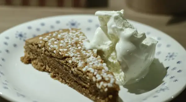 En bit glutenfri kanelbullekladdkaka med en kula vaniljglass på en tallrik med blå blommor.