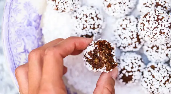 En hand håller en bit av lyxiga chokladbollar, rullade i vita pärlsocker.