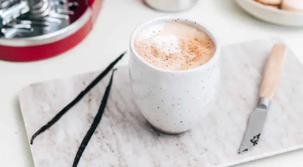 En krämig vaniljlatte hemma, med vaniljstänger och en liten kniv på en marmorerad bricka.