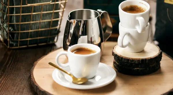 Två koppar espresso och en mjölkkanna på en träskiva. Perfekt för det godaste kaffet hemma.