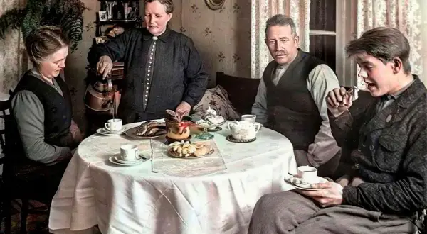 En familj samlas runt ett dukat bord för att dricka kaffe. En kvinna häller upp kaffe, en annan tittar ner, medan två män sitter och samtalar. En scen som speglar kaffe historia i Sverige.