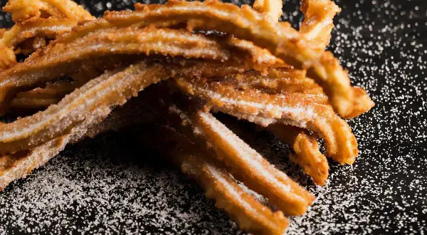 Krispiga churros, pudrade med socker, redo att avnjutas. Ett perfekt churros recept för hemmabruk.