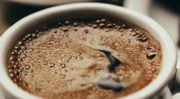 En vit kopp med bubbligt java kaffe. Skummet har regnbågsskimrande bubblor och en mörk virvel i mitten.