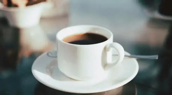 En kopp med **temp rostas** kaffe står på ett fat. I bakgrunden syns en skål med kex.