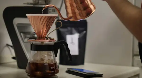En person häller varmt vatten över kaffepulver i en kopparfilterhållare för att brygga kaffe manuellt.