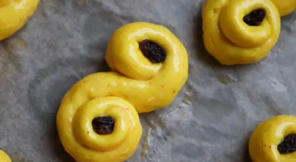 Gyllene, S-formade glutenfria bullar med russin på bakplåtspapper. Perfekt för fikat!