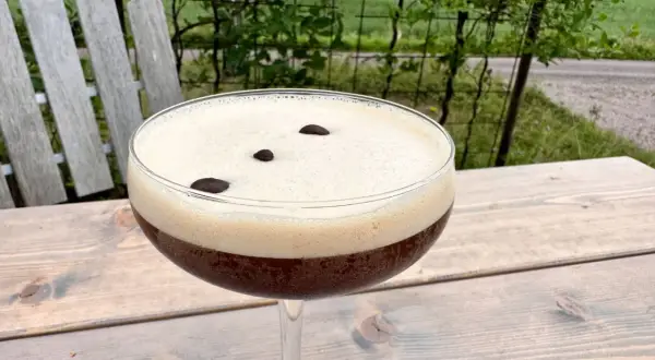 En härlig espresso martini med krämigt skum och tre kaffebönor, perfekt för en stunds avkoppling utomhus.