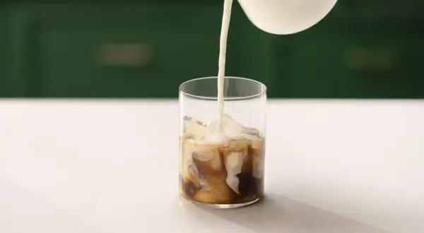 Mjölk hälls i ett glas med is och kaffe. Ett perfekt iskaffe recept för en varm dag.