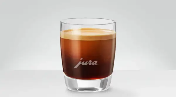 En perfekt dubbel espresso med gyllene crema i ett elegant glas med Jura-logotypen.