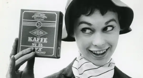 En kvinna med hatt och randig scarf håller upp en låda Löfbergs Kaffe. Kanske hon vet vilka som dricker mest kaffe i Sverige?