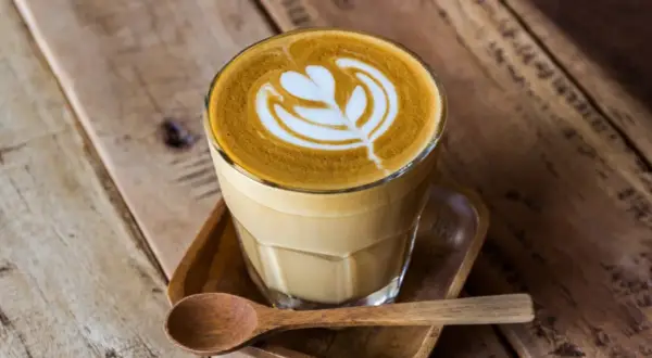 En vacker latte med mjölkskum som bildar ett mönster, serverad med en träsked. Perfekt kaffe för en mysig stund.