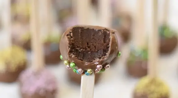 Chokladiga cake pops med färgglada strössel. En är uppäten och visar det saftiga inkråmet.