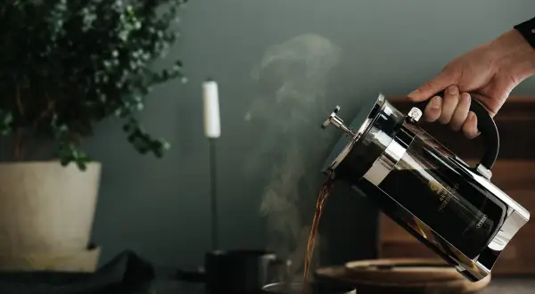 En hand häller upp ångande kaffe ur en presskanna. Perfekt presskaffe tid.