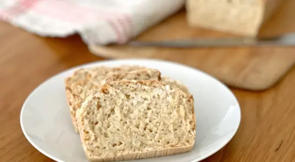 Tre skivor glutenfri limpa på en vit tallrik. En hel limpa syns i bakgrunden.