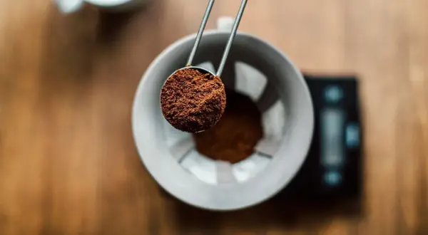 Malen kaffepulver hälls från en skopa ner i en filterhållare, redo för bryggning. Rätt kaffe temperatur är avgörande för smaken.