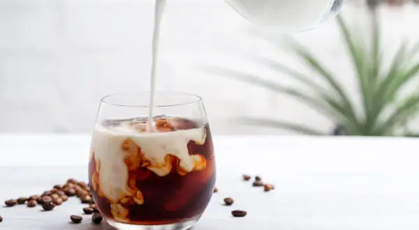 Mjölk hälls i ett glas med iskaffe och kaffebönor, en perfekt islatte.