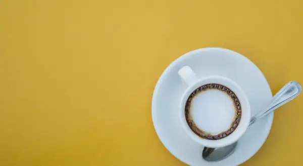 En kopp kaffe macchiato med skum och en ring av kaffe på en gul bakgrund. Perfekt för ett enkelt macchiato recept.