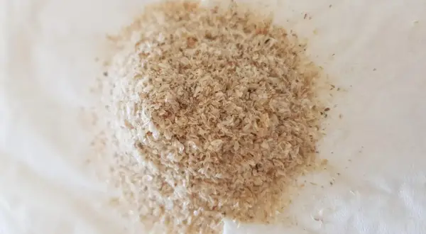 En hög med ljusbrunt fiberhusk, som ser ut som små, tunna flingor, ligger på en vit yta.