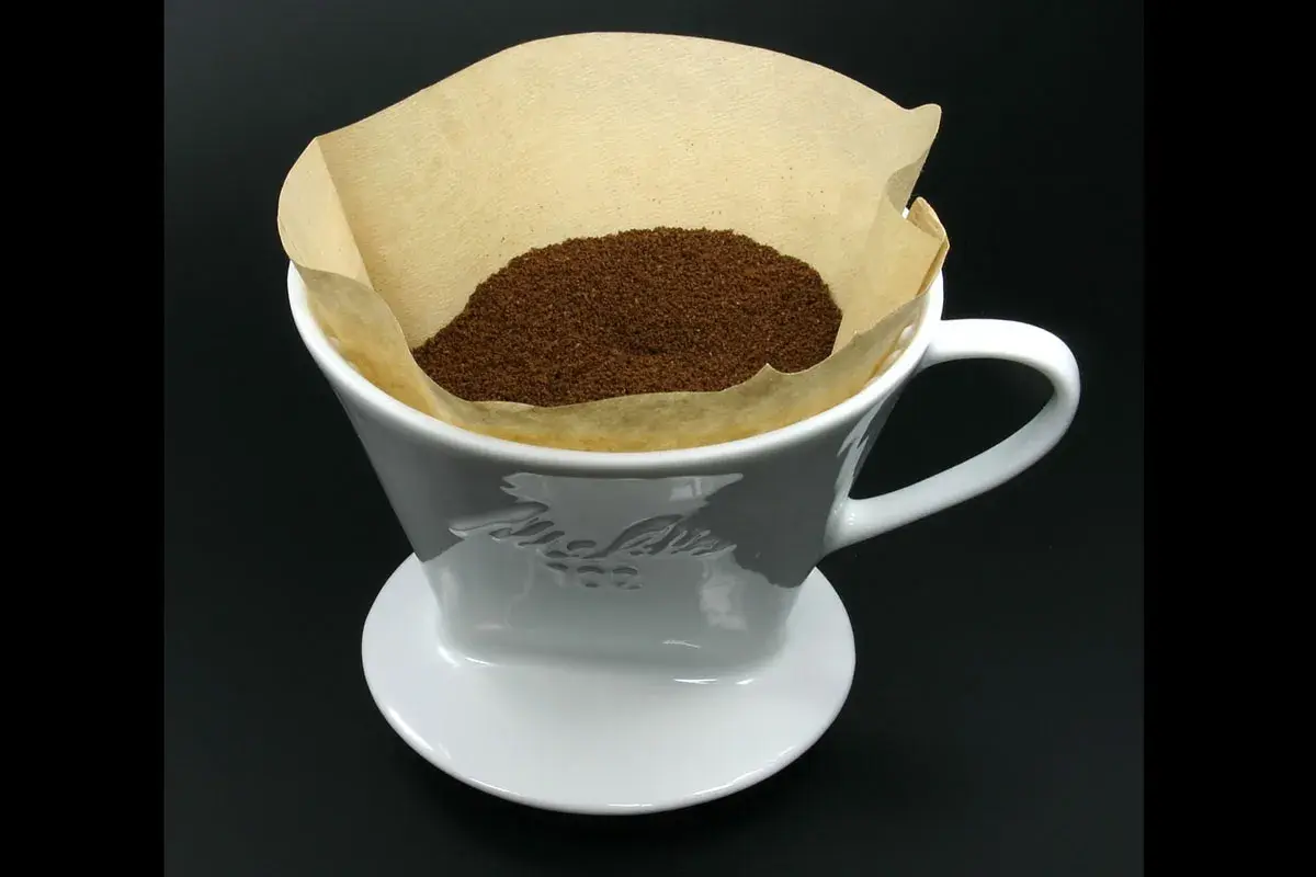 En vit kaffefilterhållare med kaffepulver i ett pappersfilter. Vem uppfann kaffefiltret? Melitta Bentz 1908.