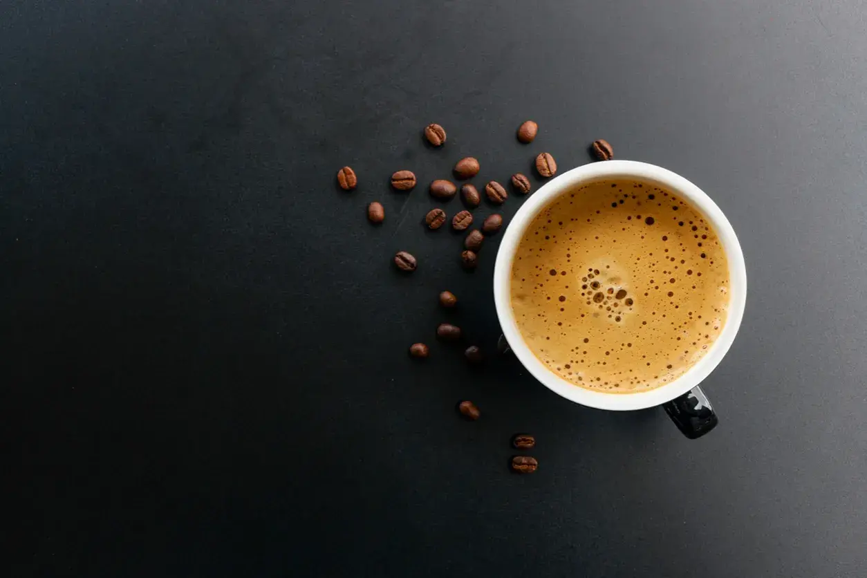 En kopp kaffe med skummig yta och kaffebönor runt omkring. Kanske någon som har en vegan i kaffet idag?