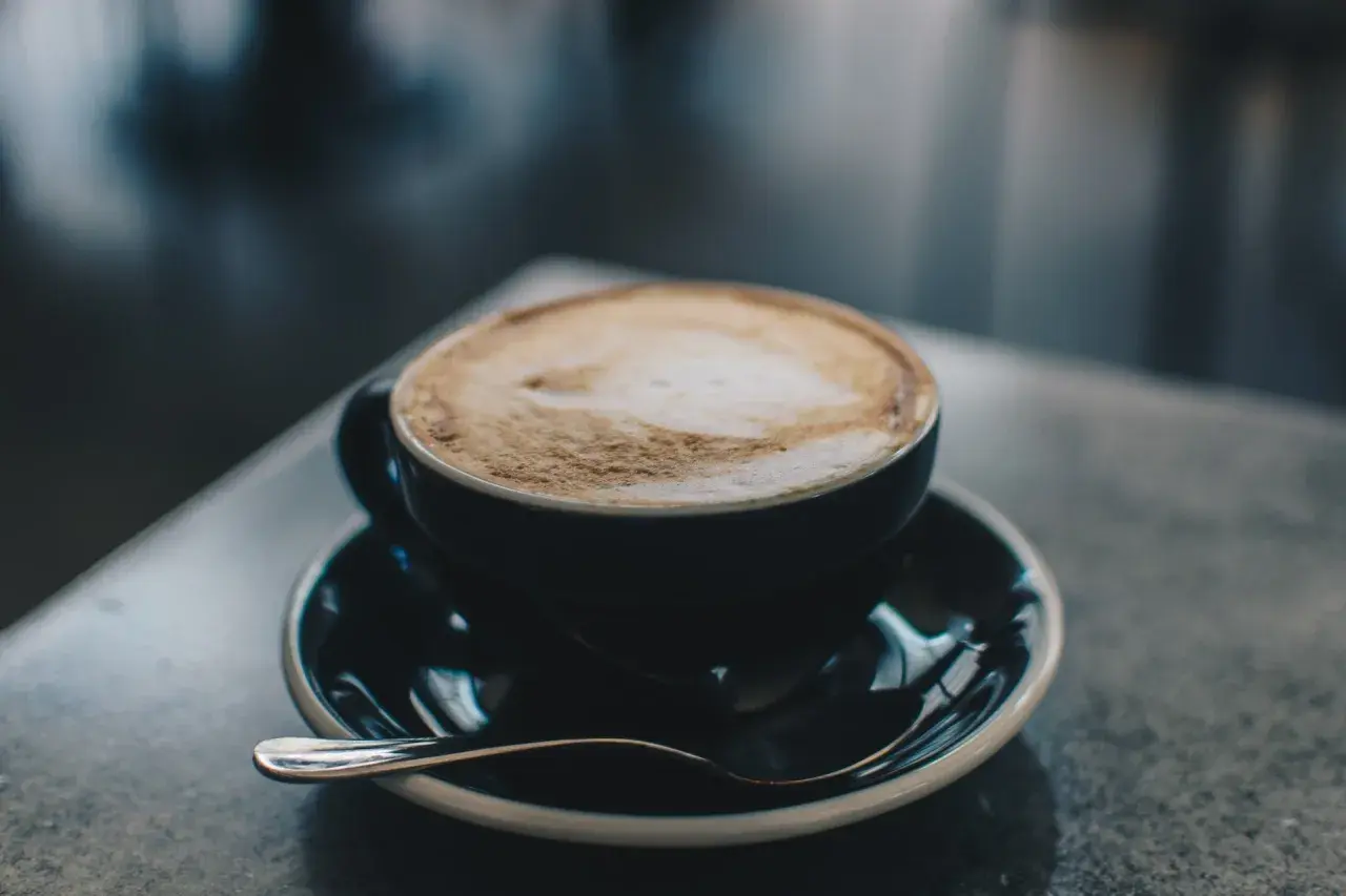 En kopp cappuccino latte med vacker skumkonst på en mörk tallrik med en sked.